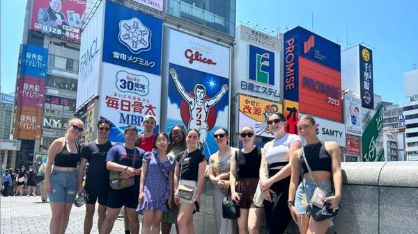 Students standing in the CBD of Osaka, Japan. Billboards stand behind them.