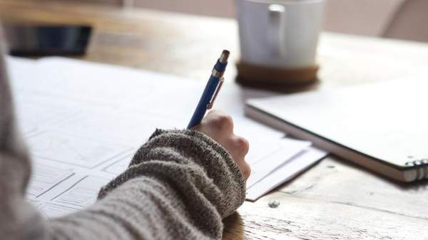 Person wearing jumper writing with pen with coffee cup in background