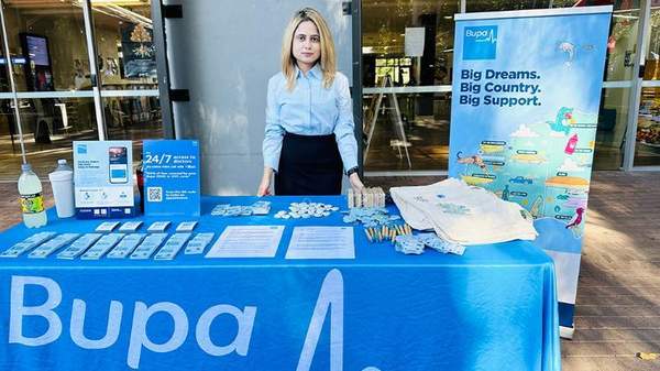 Woman stands at a stall table with Bupa items and branding displays.
