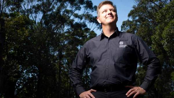 Duane Robinson looks up at a blue sky with his hands on hips. He stands in front of trees