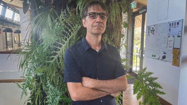 Edward Smith is indoors, standing in front of plants with his arms folded