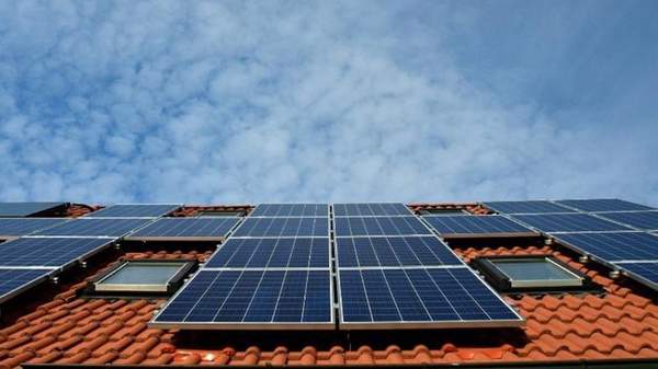 Several solar panels on a terracotta tiled roof, with a blue sky in the background