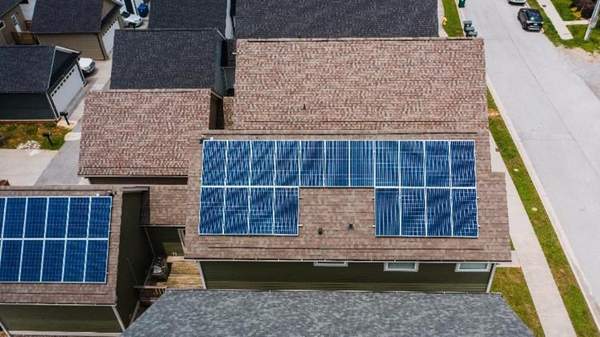 A house in suburbia with solar panels on the roof, surrounded by houses without solar
