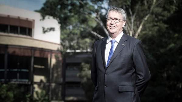 Prof Paul Wellings portrait. Brightly lit face. Wollongong Campus. Bldg 41 and gardens in background.