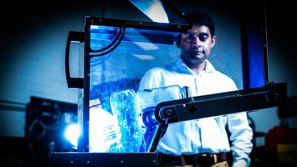 Dr Aziz Ahmed watches a machine with plastic bottles turn it into waste. He is in the background with a white shirt. Photo: Paul Jones