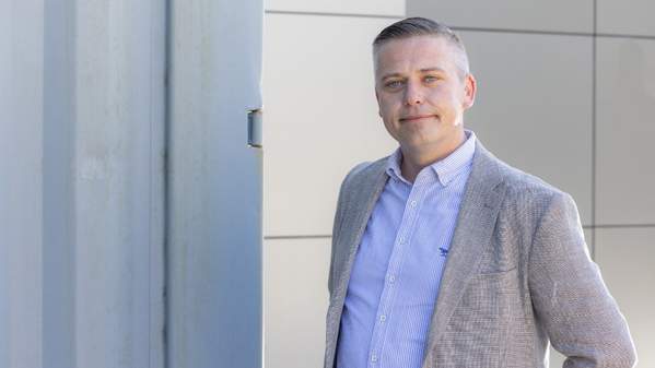 Brendan Lyon, wear a light grey suit and against a light grey background, looks at the camera with a smile. Photo: Mark Newsham