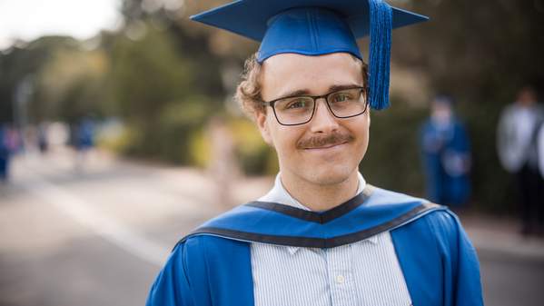 Kiarn Roughley smiles and is wearing a blue graduation cap. Photo: Michael Gray