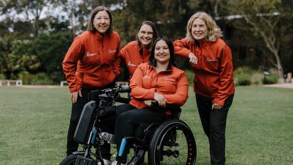 Danielle Skropeta, Tam Stutchbury, Diana King, Sharon Robinson all pose together, wearing red Homeward Bound jackets. Danielle, Tam and Sharon stand behind Diana, who is in a wheelchair. Photo: Michael Gray