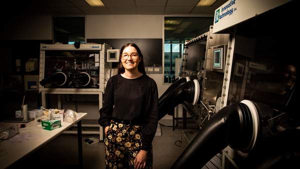 Dr Jessie Posar stands in a physics laboratory, wearing a black top and patterned pants. Photo: Paul Jones