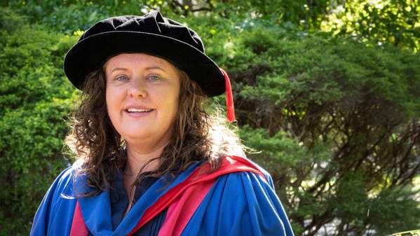 Dr Karen Tonge, wearing a black PhD cap, smiles at the camera against a background of greenery. Photo: Paul Jones