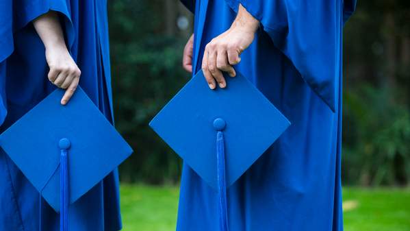 2 UOW marketing students in academic gowns and holding mortarboards