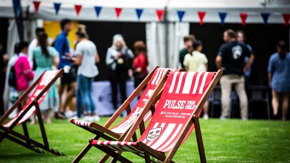 Two red and white deck chairs, with the words UOW Pulse, are in the foreground as students mingle during O Week in the background.  Photo: Paul Jones
