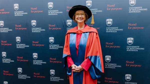 Julia Gillard wears the graduation cap and gown and stands in front of a UOW media wall, smiling. Photo: Michael Gray
