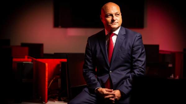 Profile photo of Professor Alex Frino. Sitting on a desk in front of computers. Red lit background.