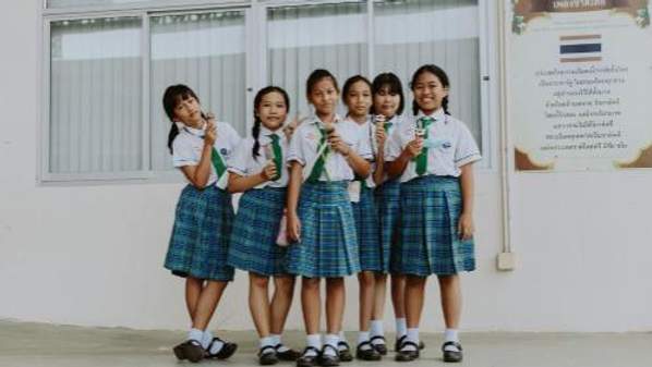 A group of six schoolgirls in uniforms stands together in front of a window, smiling and holding ice cream cones