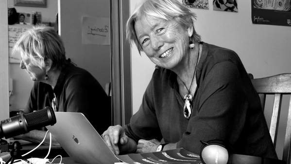 Siobhan McHugh sits at a desk, in front of a laptop with a book on the table, in this black and white image.