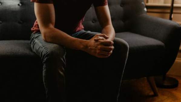 A person sitting on a sofa with clasped hands.