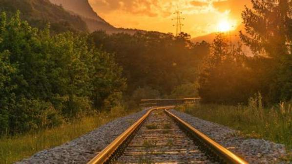 Train tracks at sunrise with hills and trees in the distance