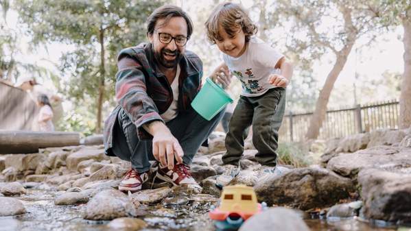 A father and son watch a boat float down a river in Early Start's Discovery Space: Photo Michael Gray