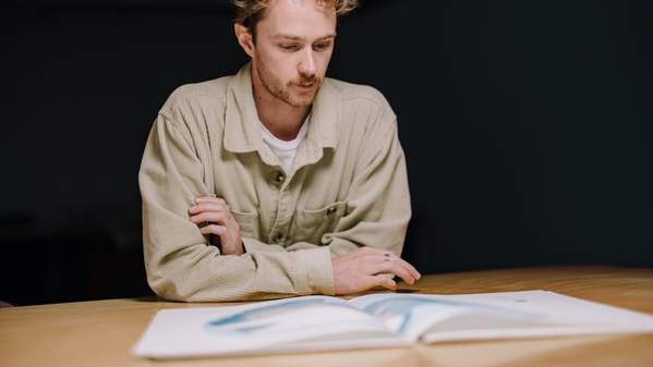 A man wears a beige jacket and sits at a table. He is peering down at a map of Antarctica. Photo: Michael Gray