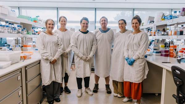 A team of researchers all wearing white lab coats stand in a row. Photo: MIchael Gray