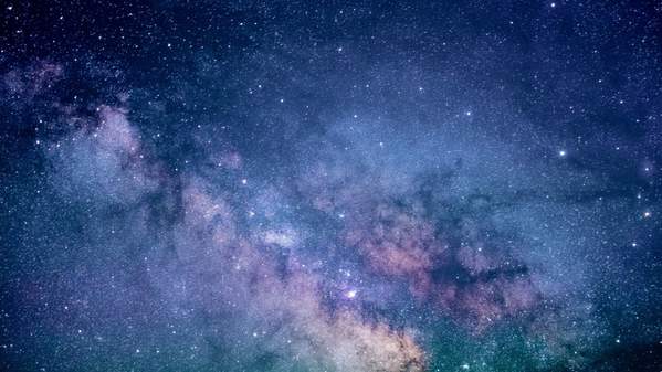 A colourful galaxy in blues, greens and purples is seen, with lots of sparkling stars. Photo: Jeremy Thomas/Unsplash