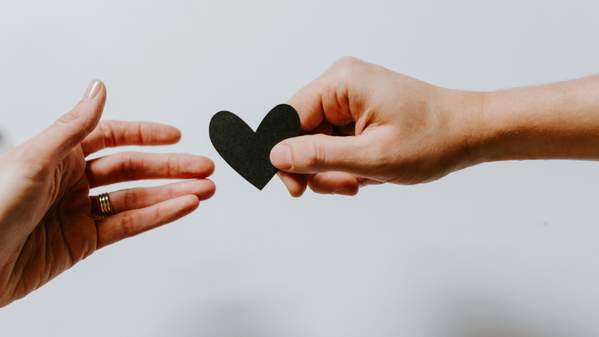 A hand gives a small black heart to another hand. Photo: Kelly Sikkema, Unsplash