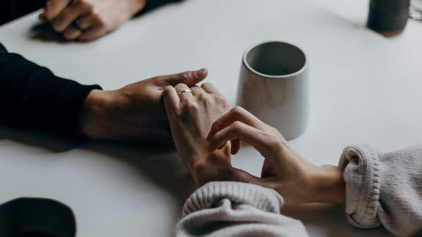 Two women hold hands across a table, next to a jug of tea. Photo: Unsplash