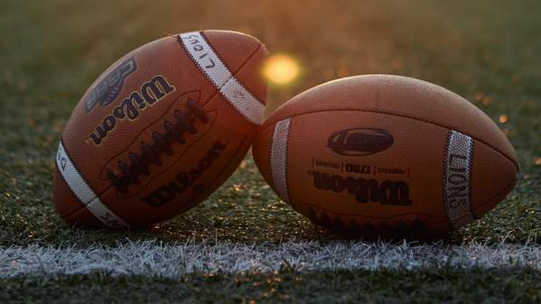 Two footballs on a playing field with a sun setting in the background. Photo: Unsplash