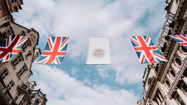 Union Jack flags are strung between two buildings, with the blue sky in the background. Photo: Unsplash