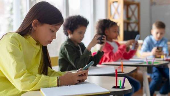 Four children sitting at desks all looking at their smart devices. Image from Shutterstock