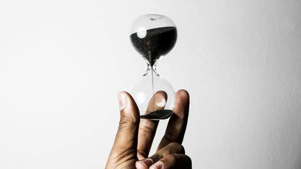 A hand holds an hourglass with black sand. Photo: Unsplash