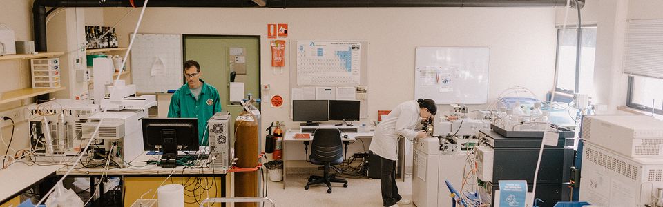 A laboratory setting with multiple computers and scientific equipment, where one person works at a workstation while another stands nearby.