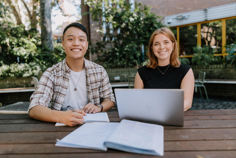 Two students sitting at a table smiling while studying