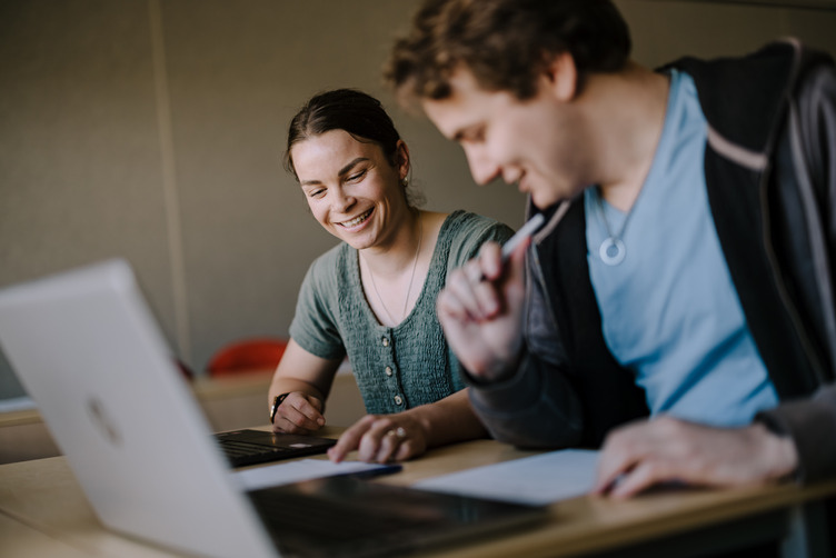 Two students sitting at table with laptop open in front