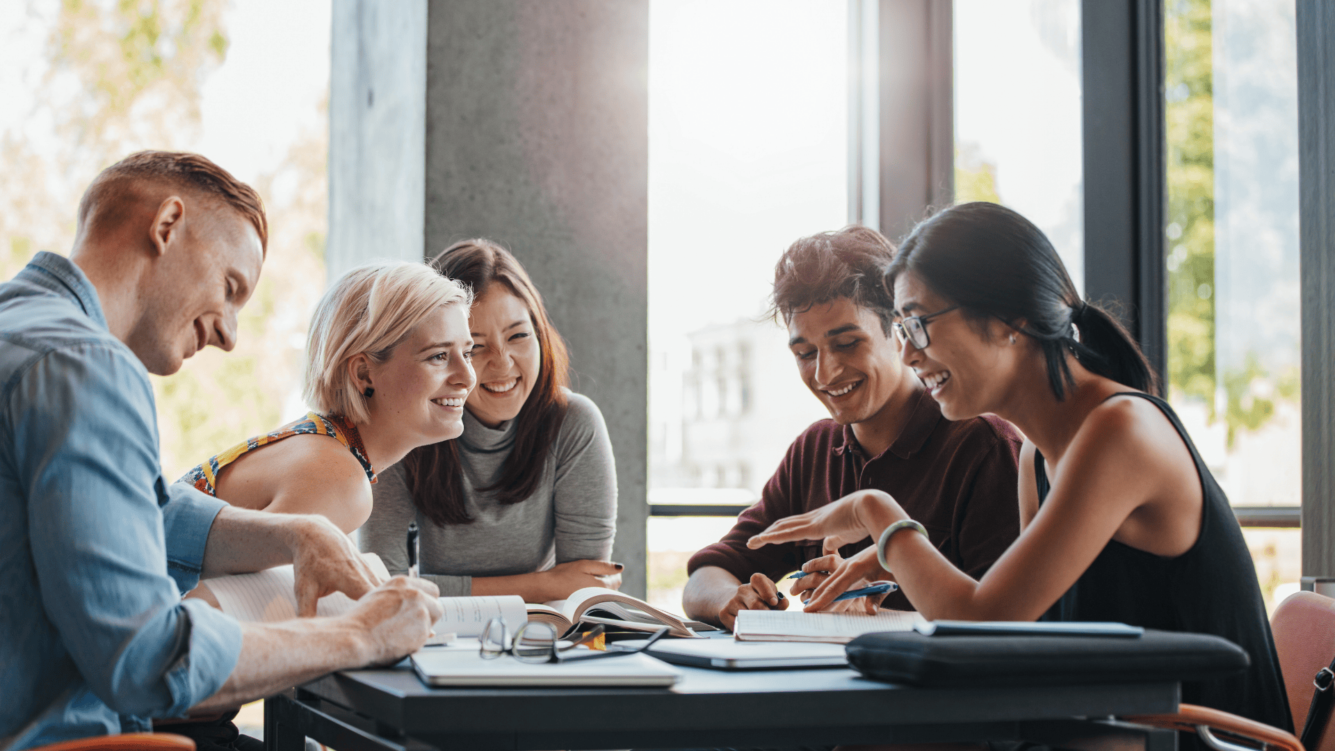 5 students sitting around a study table laughing