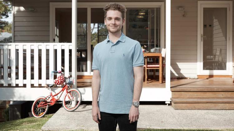 male student standing outside a house