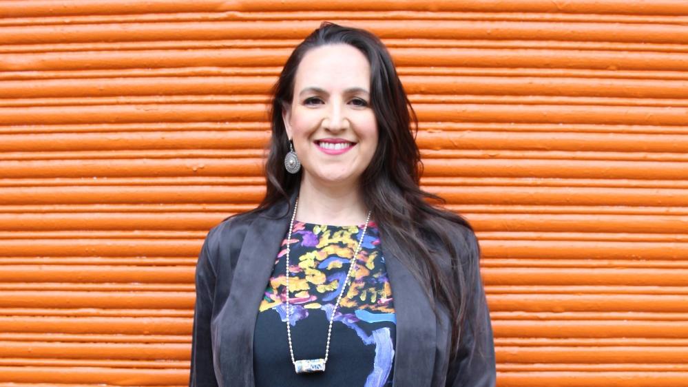 Dr Virginia Keft smiling at camera with orange backdrop