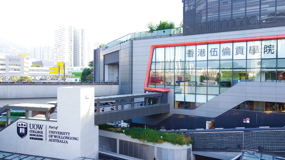 Exterior view of UOW College Hong Kong, a contemporary multi-storey campus building featuring a glass façade, grey cladding and elevated pedestrian walkways. Large Chinese characters are displayed across the front windows, while signage in the foreground reads “UOW College Hong Kong, Part of University of Wollongong Australia."