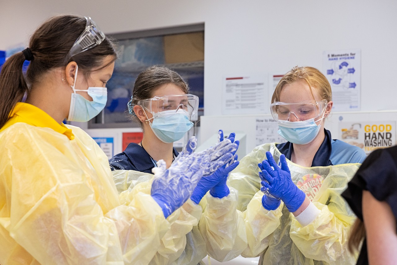 three female primary age students in scrubs and masks