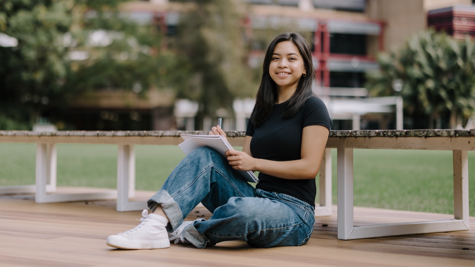 student sitting down and smiling at camera holding notepad
