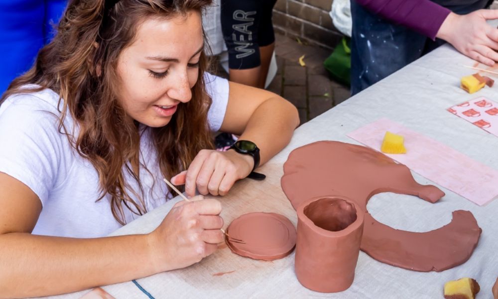 Young lady kneels at desk, while creating a vase made of clay