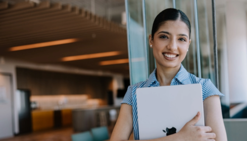 Girl holding macbook and smiling outside of a buidling