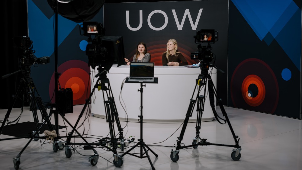 Two women sit behind a news desk with