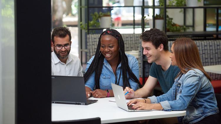 Four people sitting and smiling as they look at a laptop