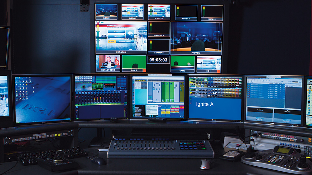 Broadcast control room with multiple monitors displaying live video feeds, production software, and broadcast controls.