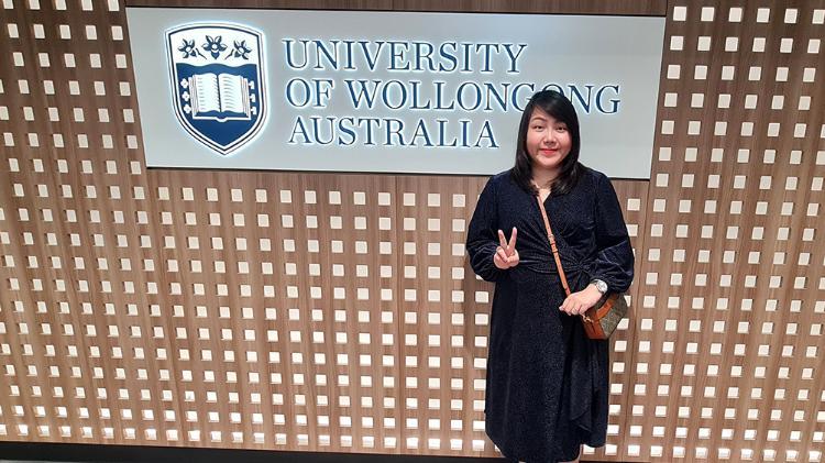 Sydney Business School, UOW student, Nitchanunt Chitruttanarut stands in front of the University of Wollongong Australia signage.