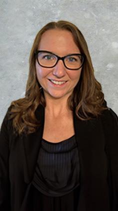 Kylie Gillett portrait. Kylie wears a black coat and top in front of a grey concrete backdrop