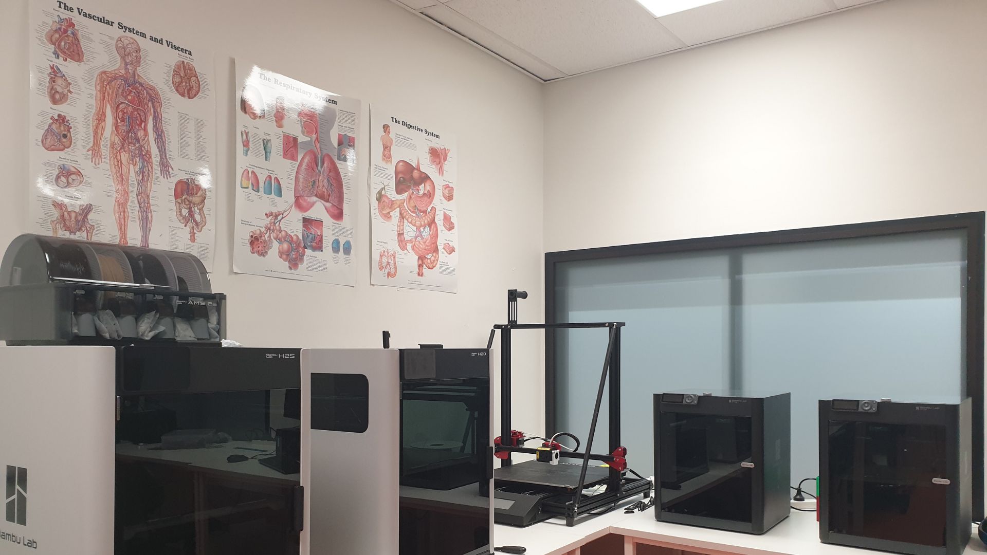 Biomedical Engineering room equipped with multiple 3D printers and anatomical posters on the wall, including diagrams of the vascular, respiratory, and digestive systems.
