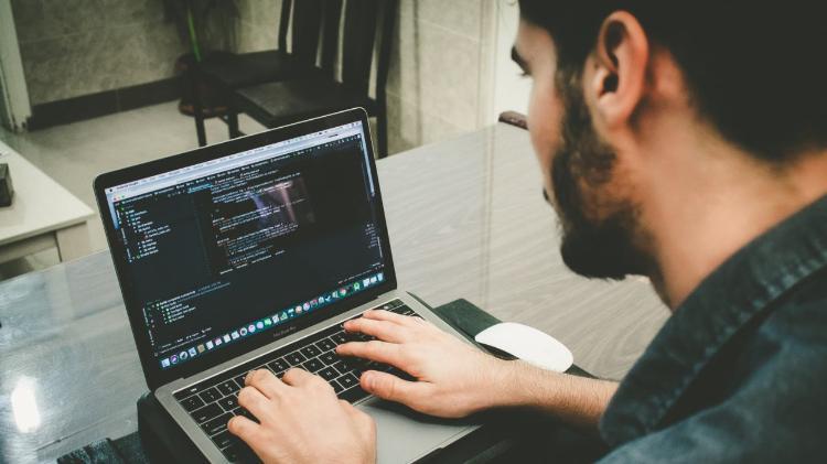 A male is sitting at a laptop typing computer code